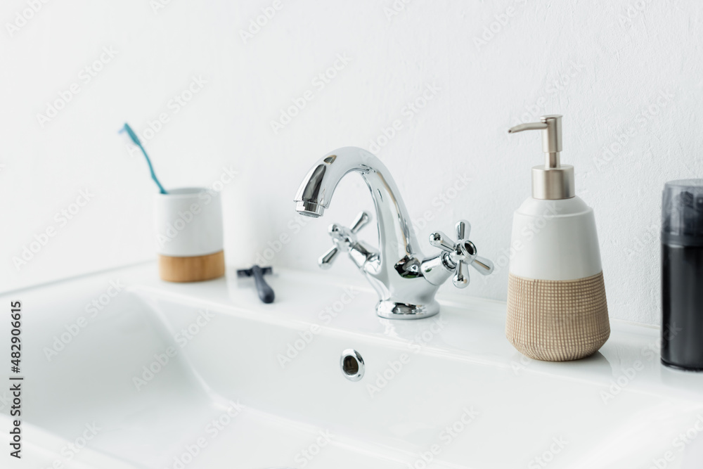 shaving foam, liquid soap, safety razor and toothbrush on white sink with faucet. shaving foam, liquid soap, safety razor and toothbrush on white sink with faucet.