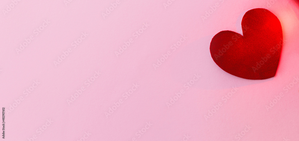 Happy Valentines Day banner. Love concept. Stylish valentine heart in red light on pink background, flat lay with space for text. Valentines day card template. Velvet heart on pink paper.
