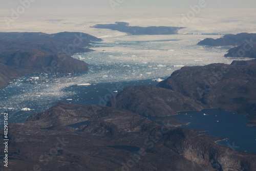 poszarpane surowe i skaliste wybrzeże Grenlandii oraz morze pokryte krą lodową widziane z samolotu z dużej wysokości