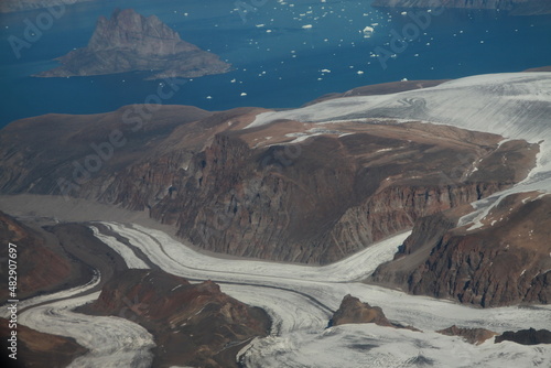 górzyste wybrzeże grenlandii pokryte topniejącym śniegiem i lodem oraz morze pokryte krą widziane z samolotu © KOLA  STUDIO