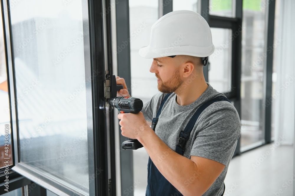 Construction worker using drill while installing window indoors Construction worker using drill while installing window indoors