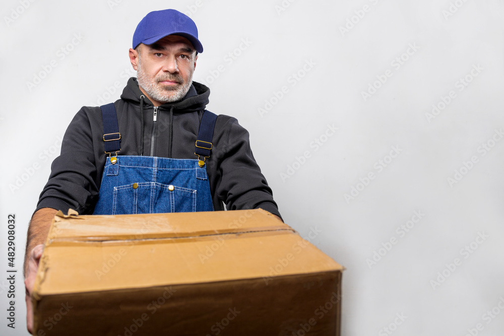 Portrait of a man in overalls with a cardboard box. Bluecollar man Portrait of a man in overalls with a cardboard box. Bluecollar man