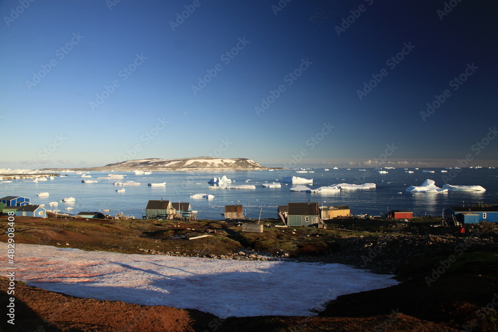 małe czerwone domki w miasteczku u wybrzeży grenlandii oraz morze arktyczne z górami lodowymi i krą w tle