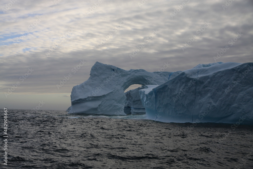 masywna góra lodowa z naturalnie wyżłobionym tunelem u wybrzeży grenlandii - obrazy, fototapety, plakaty 