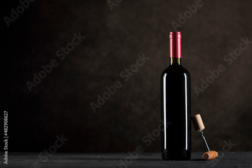 Red Wine bottle and corkscrew on a dark background with copy space © nikilitov