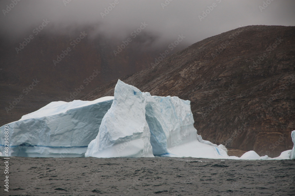 majestatyczna góra lodowa u wybrzeży grenlandii z naturalnie powstałym w niej odłamem w kształcie łuku - obrazy, fototapety, plakaty 