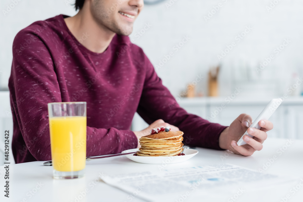 cropped view of smiling man using smartphone near pancakes and orange juice. cropped view of smiling man using smartphone near pancakes and orange juice.