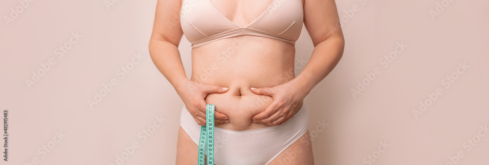 Fat woman, fat belly, plump, obese woman holding excess belly fat with measuring tape on beige background, female diet lifestyle concept - obrazy, fototapety, plakaty 