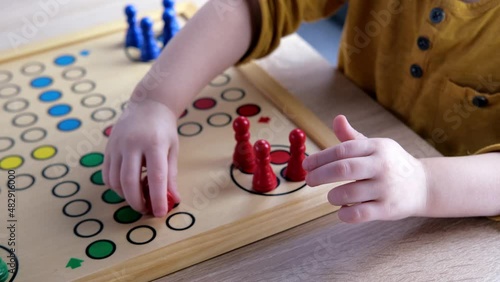 close-up of hands of small child manipulate with wooden figurines of family board game, smart kid, 2-year-old girl is learning to count, Cross and circle game Parcheesi, foreground focus photo
