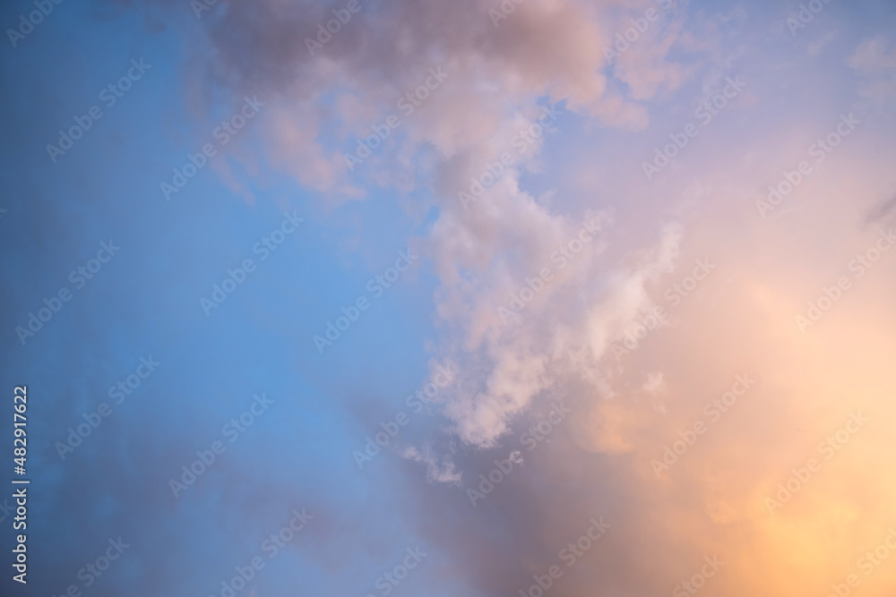 Dramatic moody sunset landscape with puffy clouds lit by yellow setting sun and blue sky.