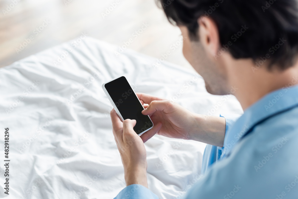 blurred man holding mobile phone with blank screen in bedroom.