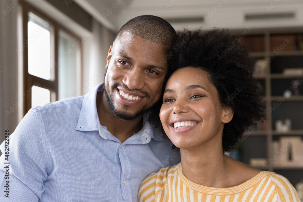 Handsome bearded husband and beautiful curly-haired wife standing in modern room smiling looking at camera, having wide toothy smile, African couple close up portrait. Love, romantic dating concept Handsome bearded husband and beautiful curly-haired wife standing in modern room smiling looking at camera, having wide toothy smile, African couple close up portrait. Love, romantic dating concept