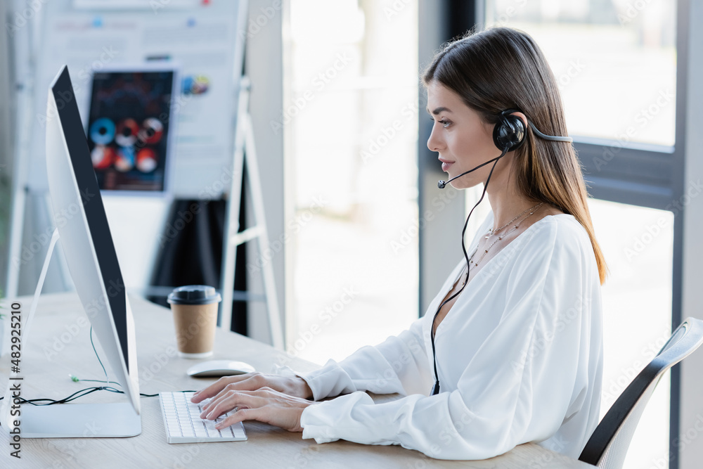 side view of young woman in headset typing on computer keyboard in office. side view of young woman in headset typing on computer keyboard in office.