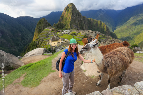 Young woman standing with friendly llamas at Machu Picchu overlook in Peru photo
