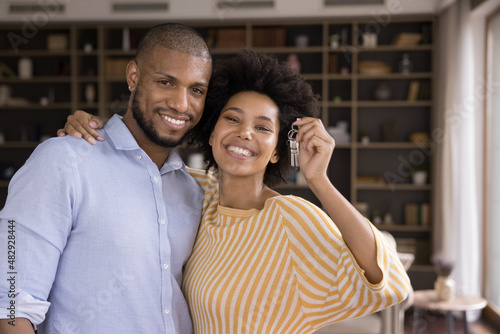 Happy homeowners couple portrait, bank loan for young family, relocation, accommodation, travel concept. Beautiful African spouses smiling, showing at camera bunch of keys from their new first house