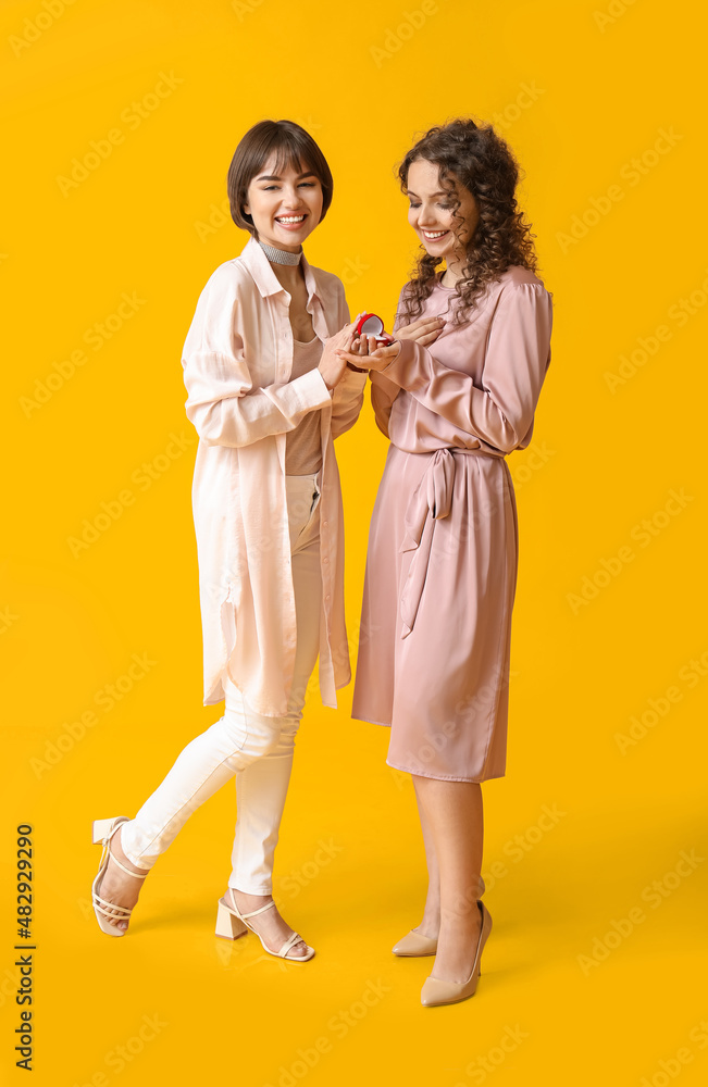 Young lesbian woman proposing to her girlfriend on color background Young lesbian woman proposing to her girlfriend on color background