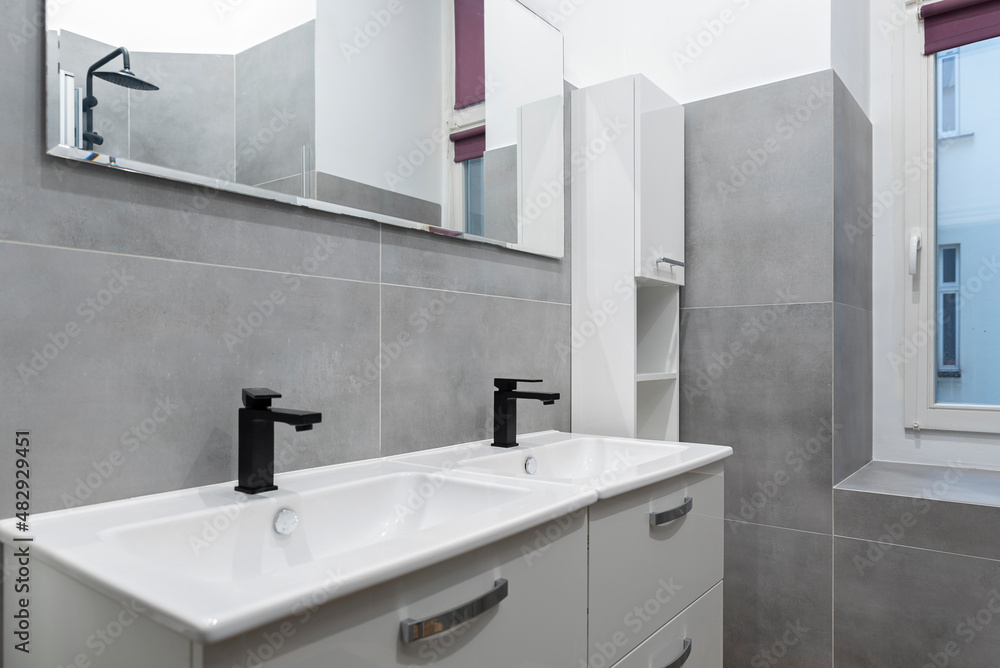 Double sink in bathroom. Ceramic washbasin in wasroom with grey tiles and mirror in stylish interior in hotel. Double sink in bathroom. Ceramic washbasin in wasroom with grey tiles and mirror in stylish interior in hotel.