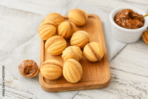 Board of tasty walnut shaped cookies with boiled condensed milk on light wooden background