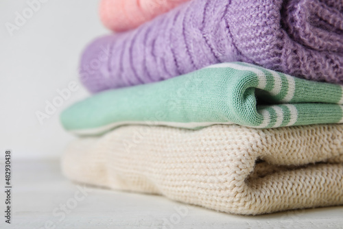 Stylish baby sweaters on light wooden table, closeup