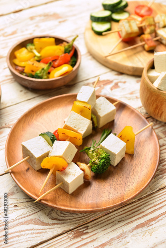 Plate with grilled tofu cheese skewers on light wooden background, closeup