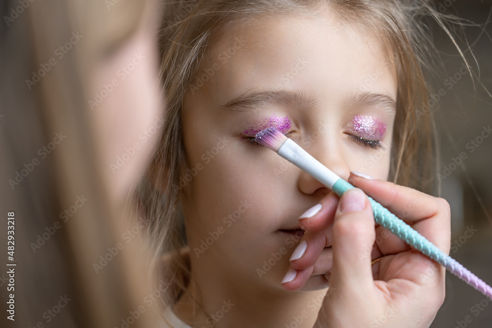 mom uses a brush to apply shiny shadows on eyelids of her daughter mom uses a brush to apply shiny shadows on eyelids of her daughter
