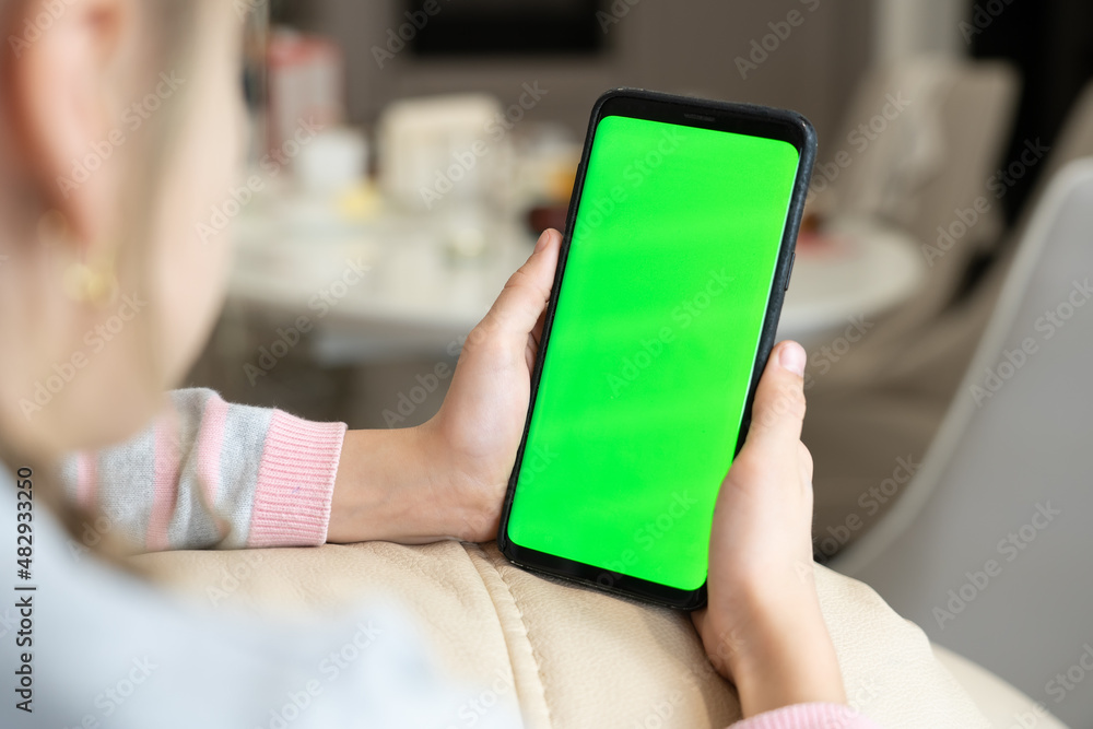 Little girl use smart phone with blank green screen mock up display for advertising text while rest on couch in living room at modern home. Phone with green screen and chroma key for copy space Little girl use smart phone with blank green screen mock up display for advertising text while rest on couch in living room at modern home. Phone with green screen and chroma key for copy space