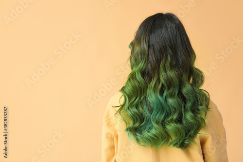Beautiful young woman with unusual green hair on color background