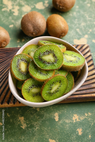 Bowl with slices of fresh kiwi on green background