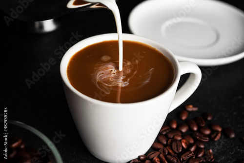 Coffee americano with milk in cup and saucer isolated on dark background. Hot coffee