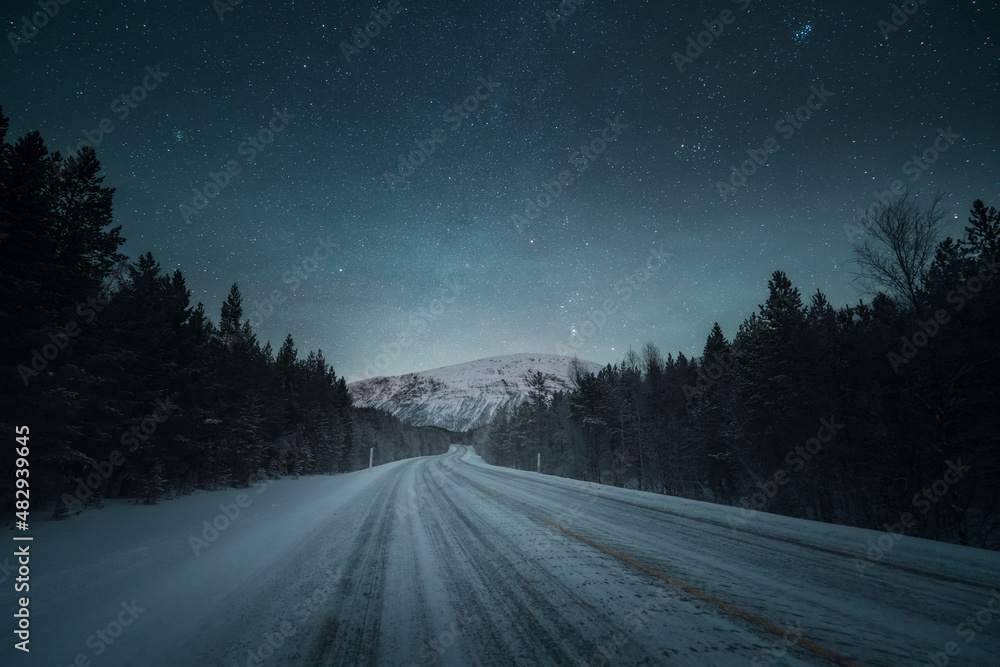 A night road and beautiful scenery with starry night sky. Winter landscape with empty road, forest and mountains. . High quality photo