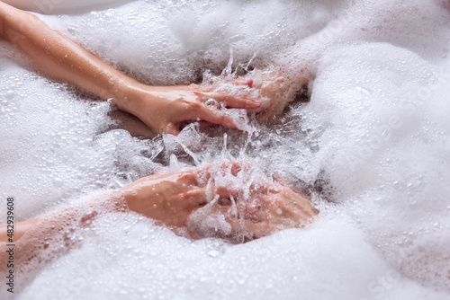 Close up top view of the hands of a couple in love taking a bath together with white foam. Lovers shake the water with soap to form foam. Newlyweds have fun on honeymoon weekend morning. Hand hygiene