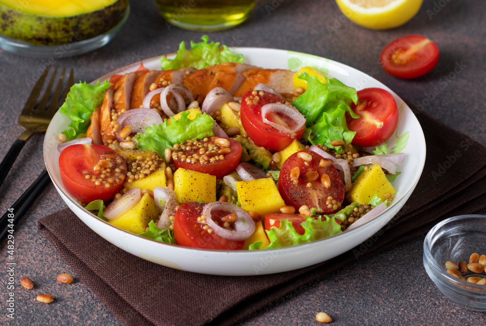 Salad with mango, smoked chicken and cherry tomatoes served with green lettuce leaves in a plate on a brown background Salad with mango, smoked chicken and cherry tomatoes served with green lettuce leaves in a plate on a brown background