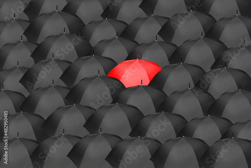 Sea of black umbrellas with one red umbrella in the center, symbolizing an idea, innovation, leadership, audacity, bravery.