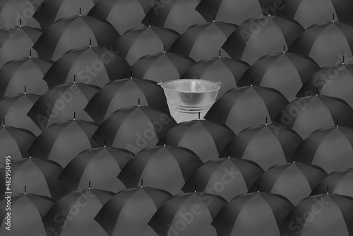 Sea of black umbrellas with a single bucket in the center catching water, symbolizing a breakthrough idea, innovation, audacity, daring, sustainability. photo