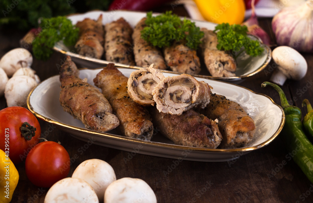 Pork rolls with mushrooms, meat rolls surrounded by greenery and vegetables. Ukrainian dishes is called krucheniki Pork rolls with mushrooms, meat rolls surrounded by greenery and vegetables. Ukrainian dishes is called krucheniki