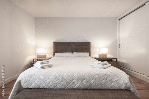 Bedroom with king size bed  matching upholstered headboard and bench and clean white towels on the bedspread