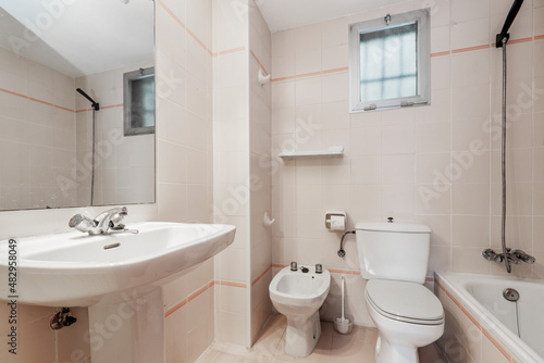 Conventional toilet with all white toilets  rectangular mirror and small window in the wall