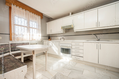 Kitchen with walls covered with white wood cabinets  white countertops and gray tiles  white marble floor and white wood corner table