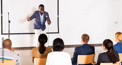 Portrait of expressive inspirational african american speaker with microphone on conference room stage during motivational coaching seminar