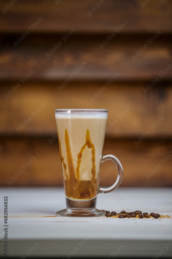 Cappucino with cinamon in tall glass on table with wood background and coffee beans