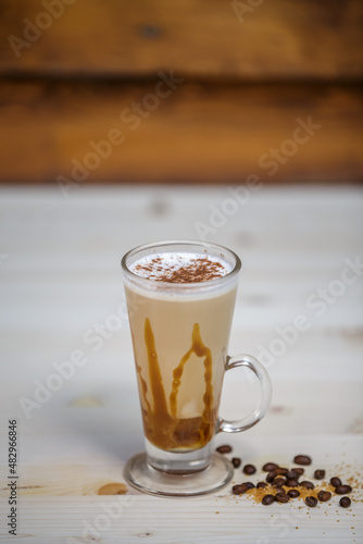 Cappucino with cinamon in tall glass on table with wood background and coffee beans