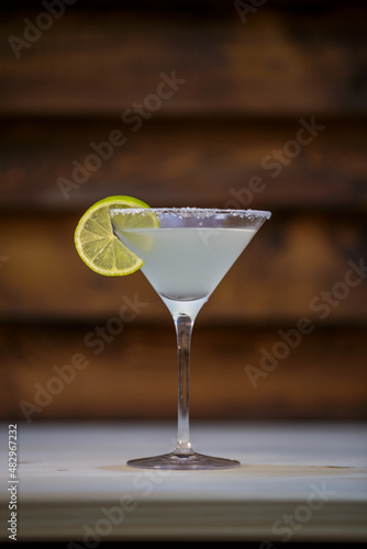 Fresh cold martini cocktail glazed and crushed ice with lime garnish on table with wood background