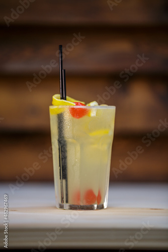 Fresh cold cocktail with lemon and cherry on table with wood background