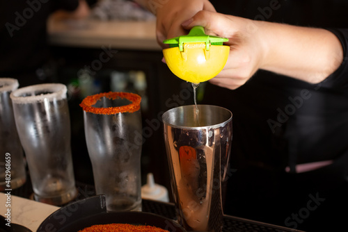 A closeup view of a bartender preparing a cocktail, using a lemon juicer tool.