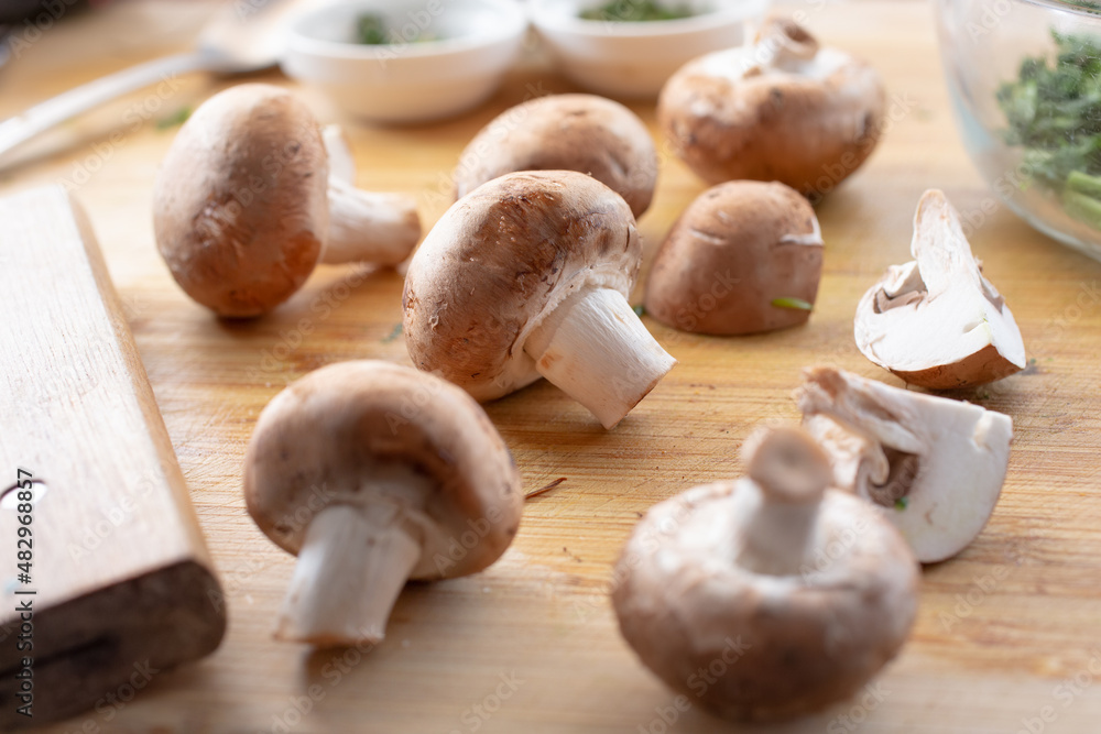 A view of several crimini mushrooms on a wooden cutting board. A view of several crimini mushrooms on a wooden cutting board.