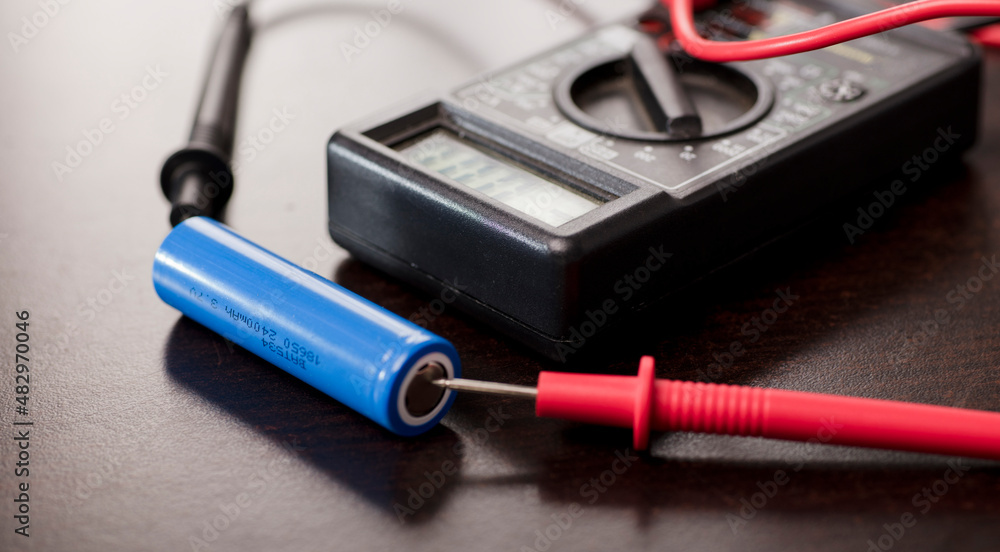 battery with volt calculator, voltmeter, red positive pole, black negative pole, on wood work table battery with volt calculator, voltmeter, red positive pole, black negative pole, on wood work table