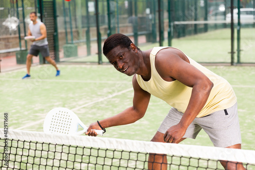 Portrait of sporty man playing with male partner padel doubles game on outdoors court © JackF