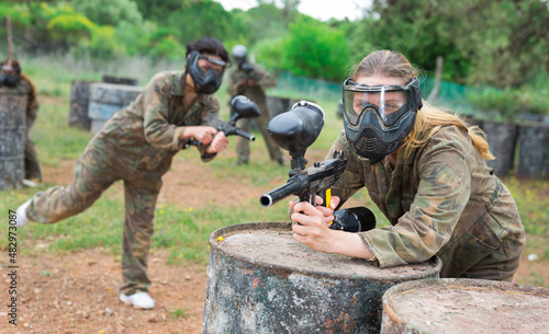 Female paintball player in protective mask with ammunition and gun on paintball field