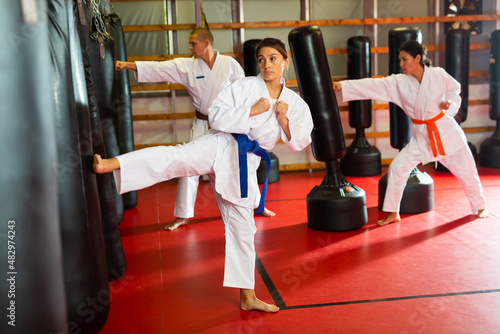 Women and man in kimono exercising with punching bags in gym during karate training. © JackF