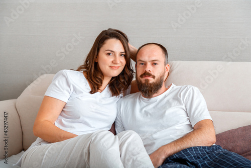 Young beautiful couple in pajamas hug while sitting on couch at cozy home interior. Married man and woman romantic relationship. Husband and wife portrait, morning routine © Beton Studio